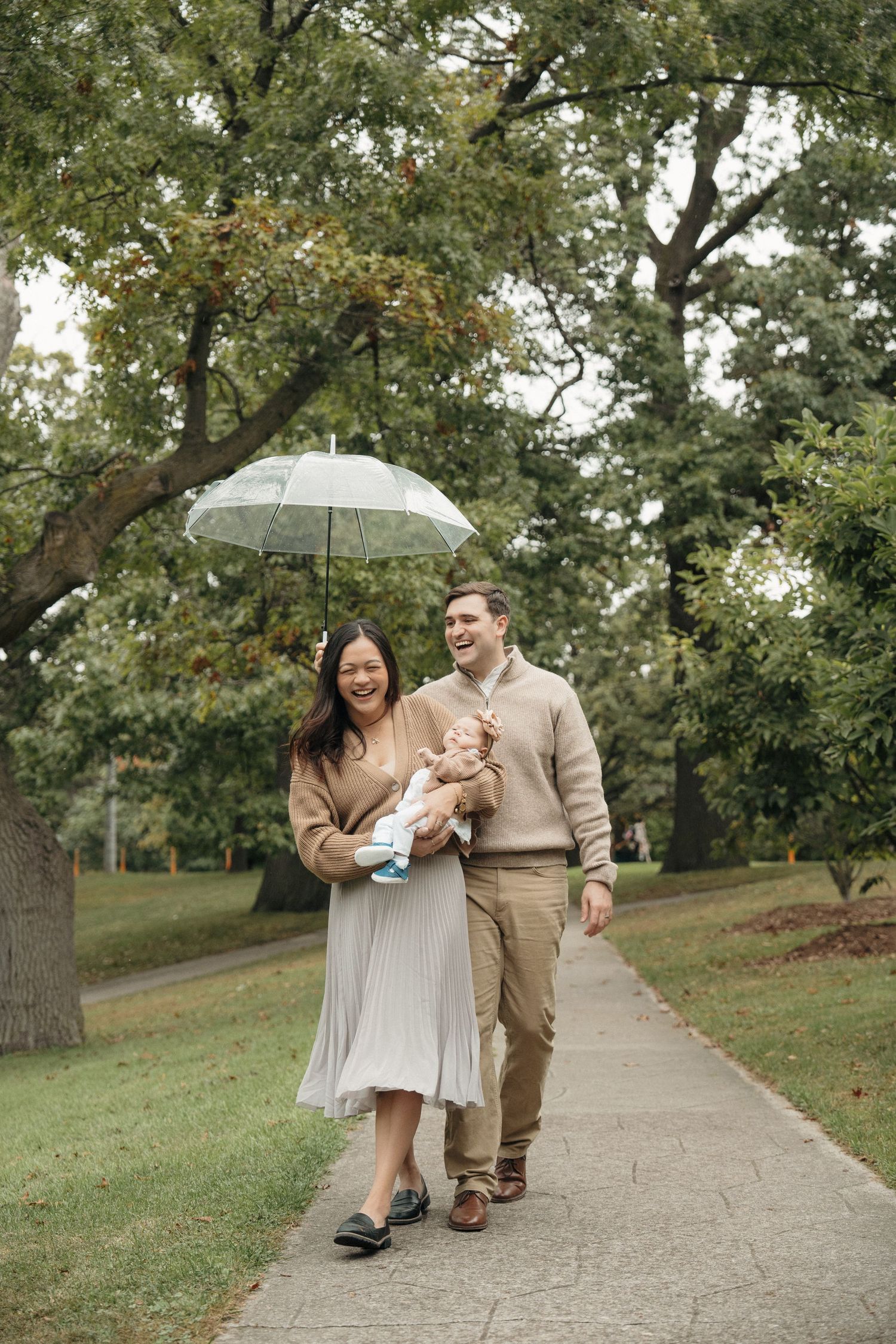 A family plays and laughs together in a park during autumn, with colorful fall foliage in the background.