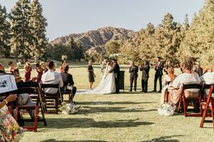Wedding ceremony outdoors with mountain views and wooden chairs set up on a grassy field in natural lighting.