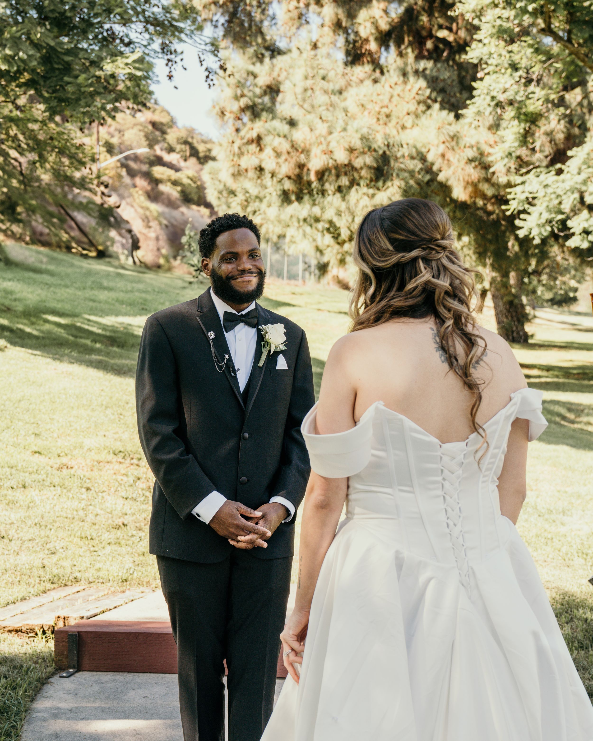 A romantic first look moment between newlyweds in a sunny outdoor garden setting with fall foliage.