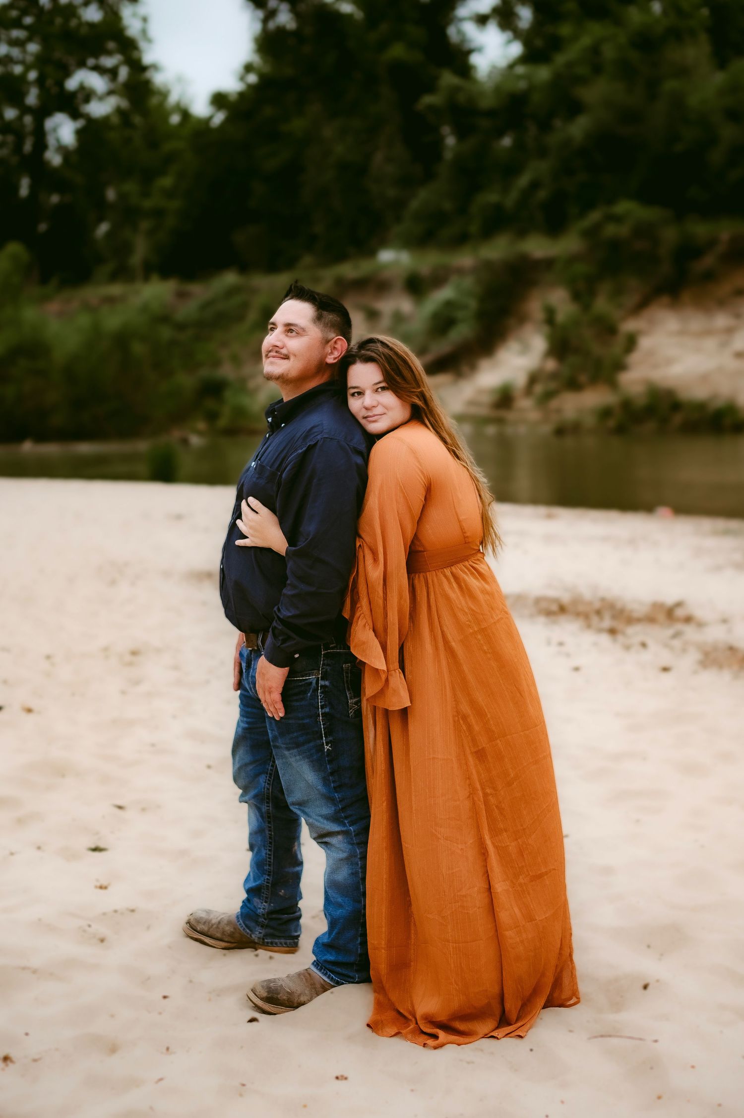 A couple shares intimate moments on a sandy beach shoreline with the person wearing a flowing burnt orange dress.