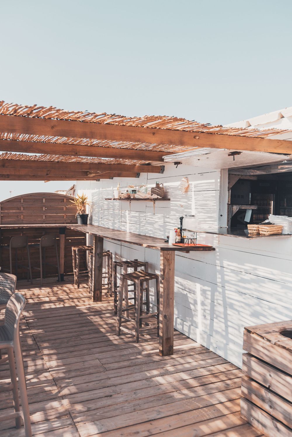 Rustic wooden deck with white walls and pergola creating dramatic shadows.