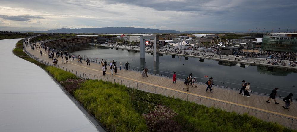 Crowds of people walking along a waterfront bridge at an outdoor event during dusk.