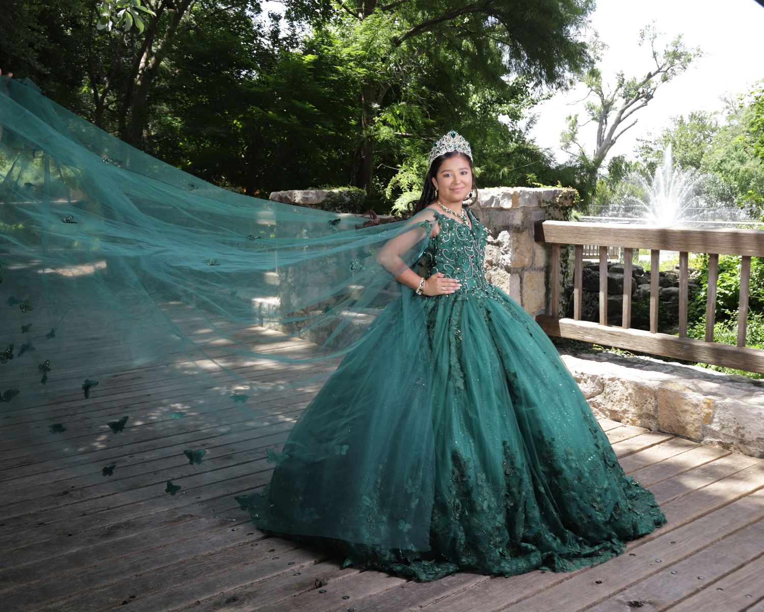 A flowing emerald green ball gown with lace details billows dramatically across a wooden deck in an outdoor setting.