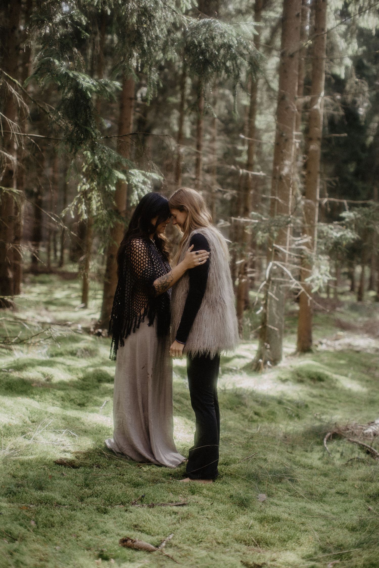 A romantic forest scene with two people embracing in a misty woodland setting wearing bohemian style clothing.