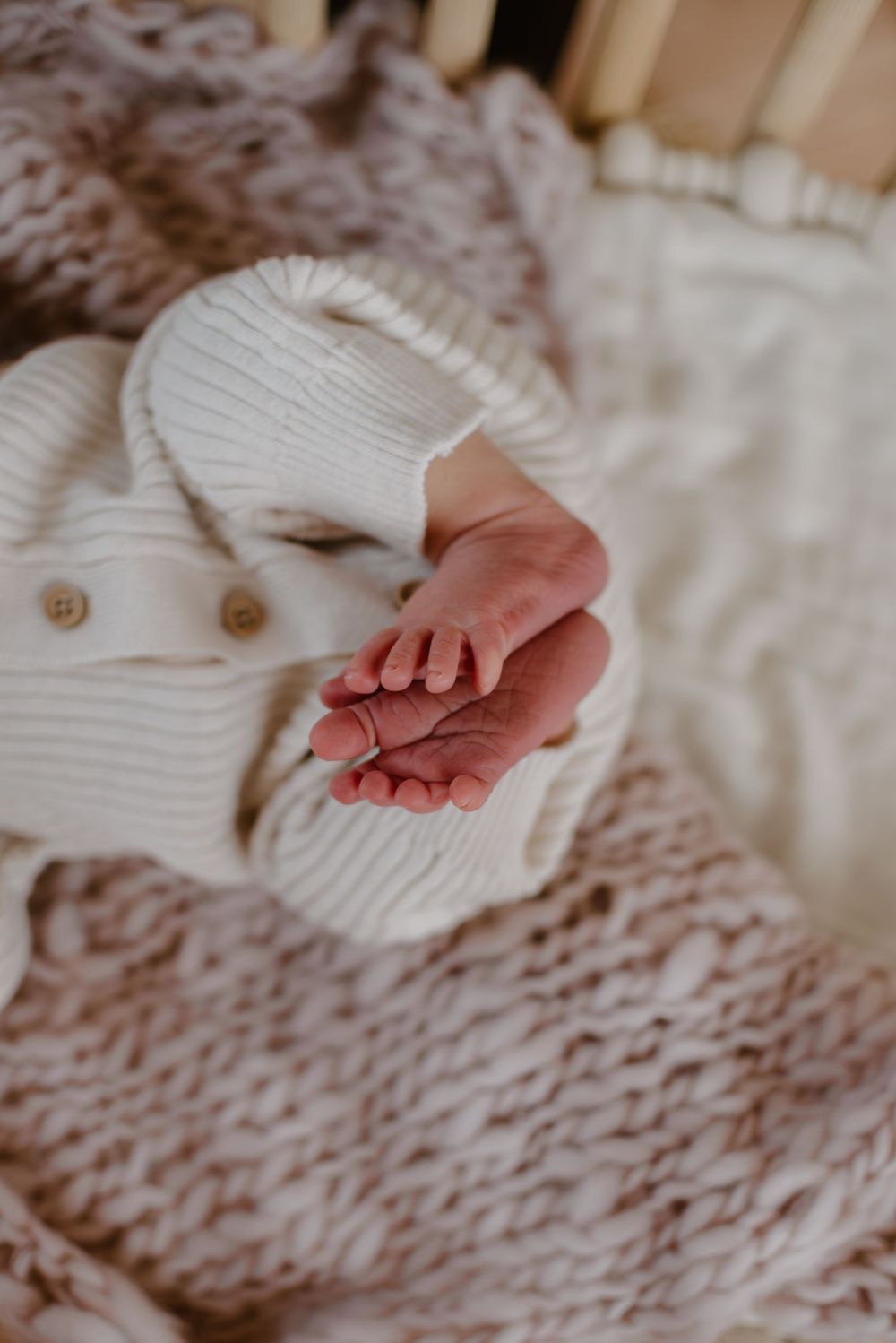 Tiny newborn feet peek out from a cozy white knit blanket on textured bedding.