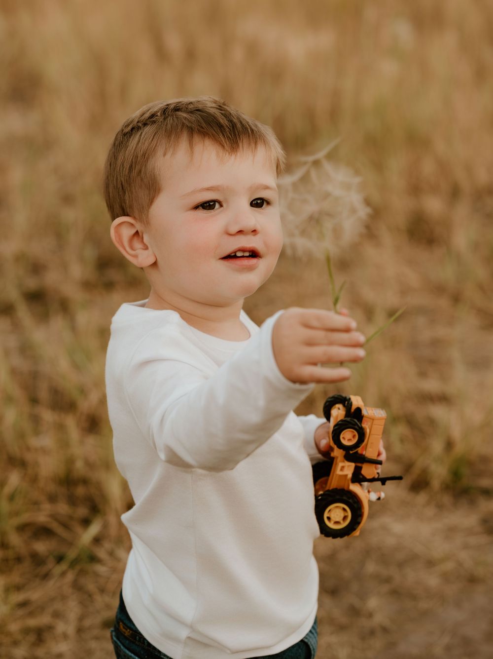 Little one in white shirt reaches up joyfully while playing outdoors in a grassy autumn field.