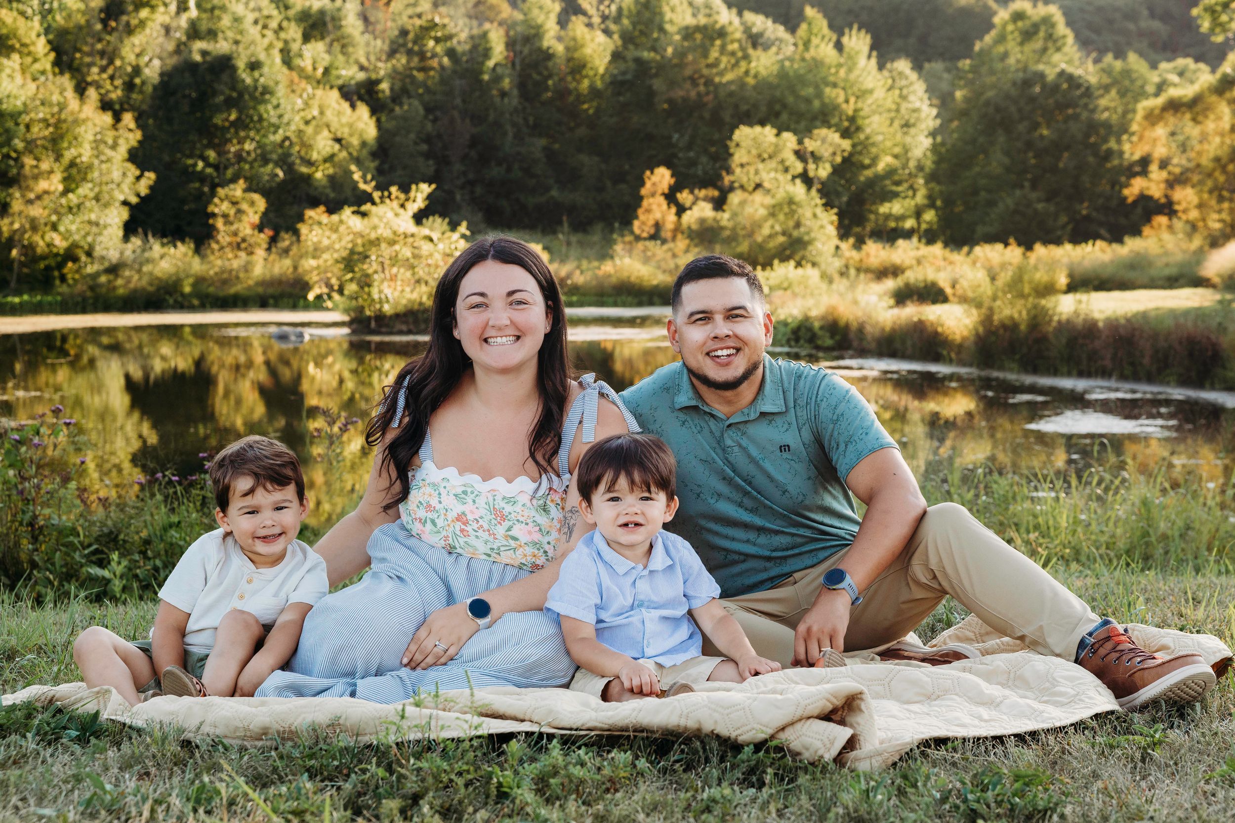 Family relaxing together on a blanket by a serene pond during golden hour in nature.