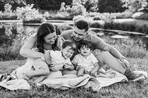 Black and white portrait of a family sharing a joyful moment while sitting on blanket near a pond.