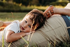 A young child rests peacefully on someone's side during a tranquil moment outdoors in golden sunlight.