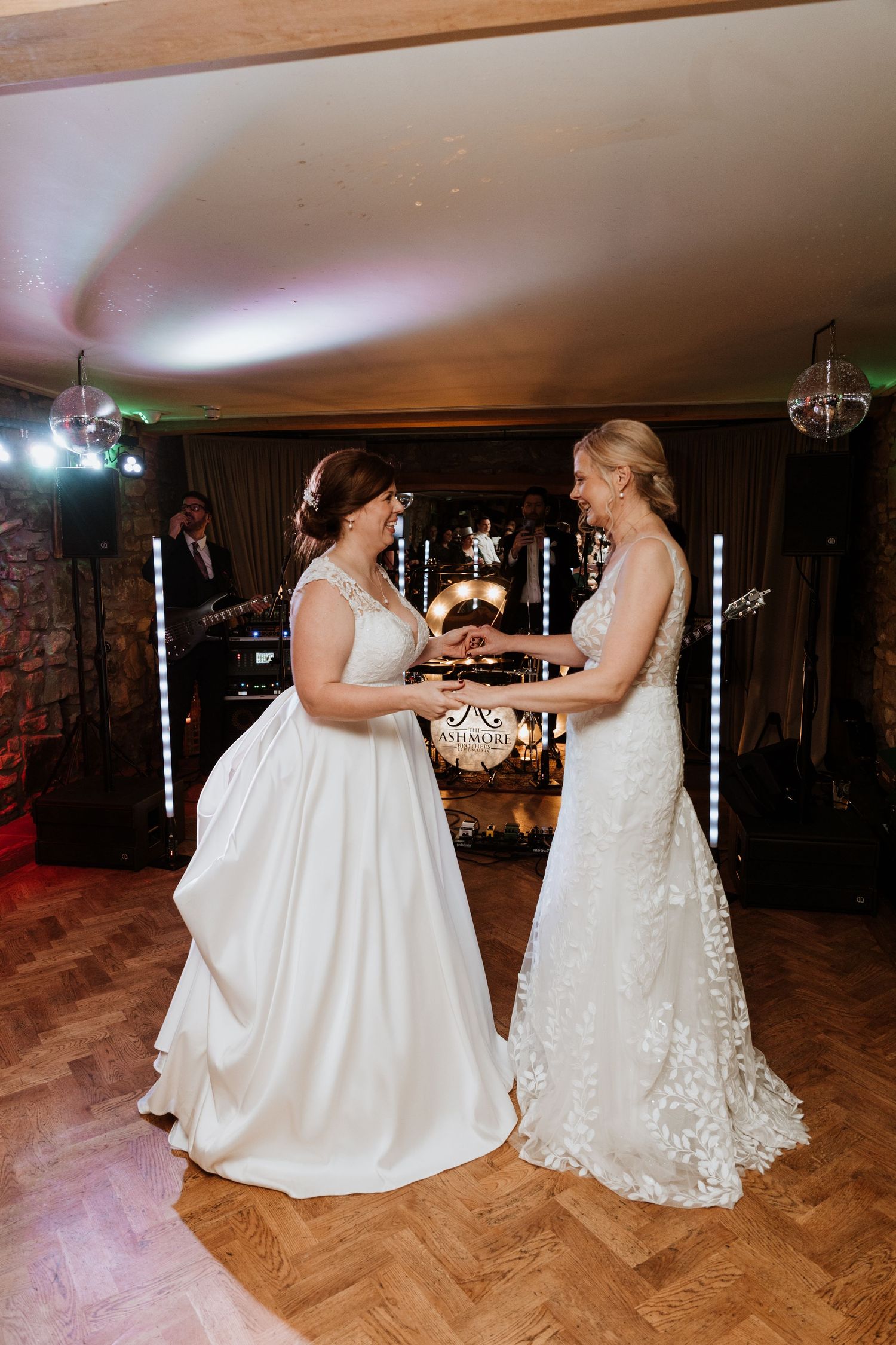 Two brides share a tender dance moment together on a wooden dance floor at their wedding reception at Tower Hill Barns