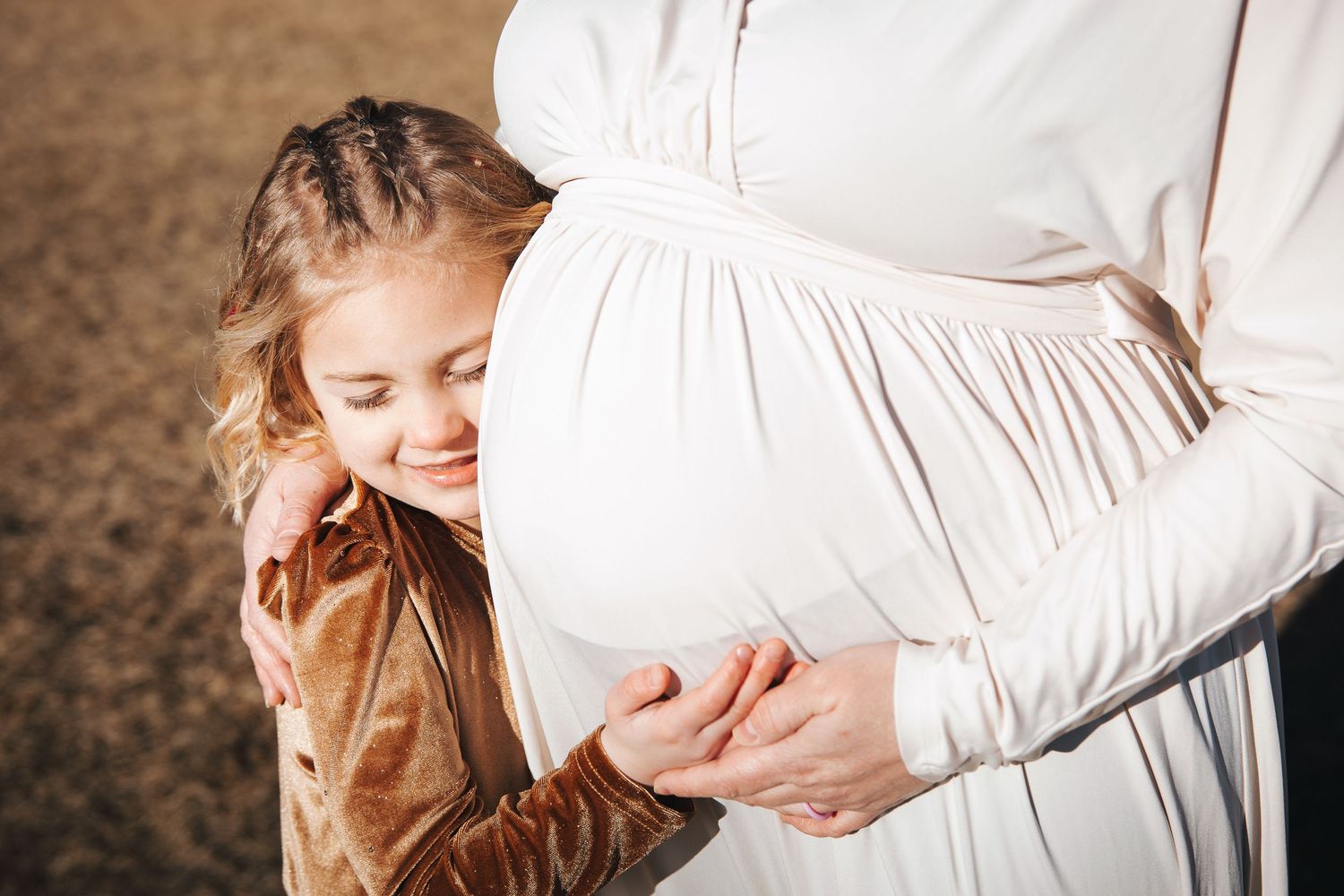 Tender maternity photo session showing gentle embraces and white flowing dress.