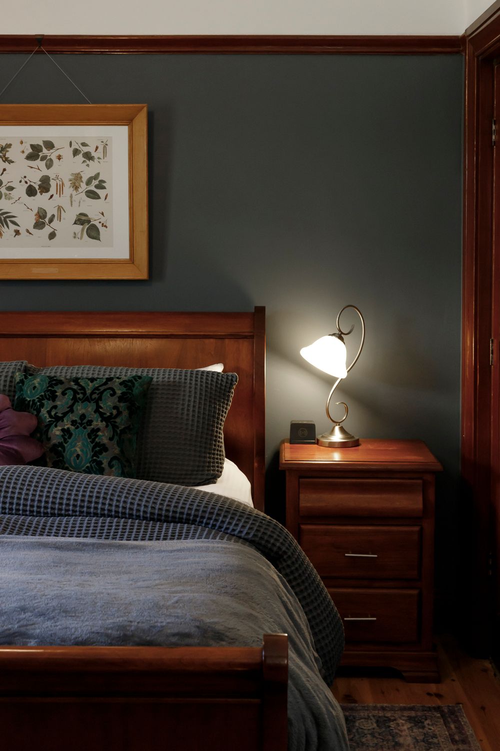Interior property photo by Em Callaghan Photography of an art deco bedroom with dark blue walls, timber trim, sleigh bed, side table & lamp.