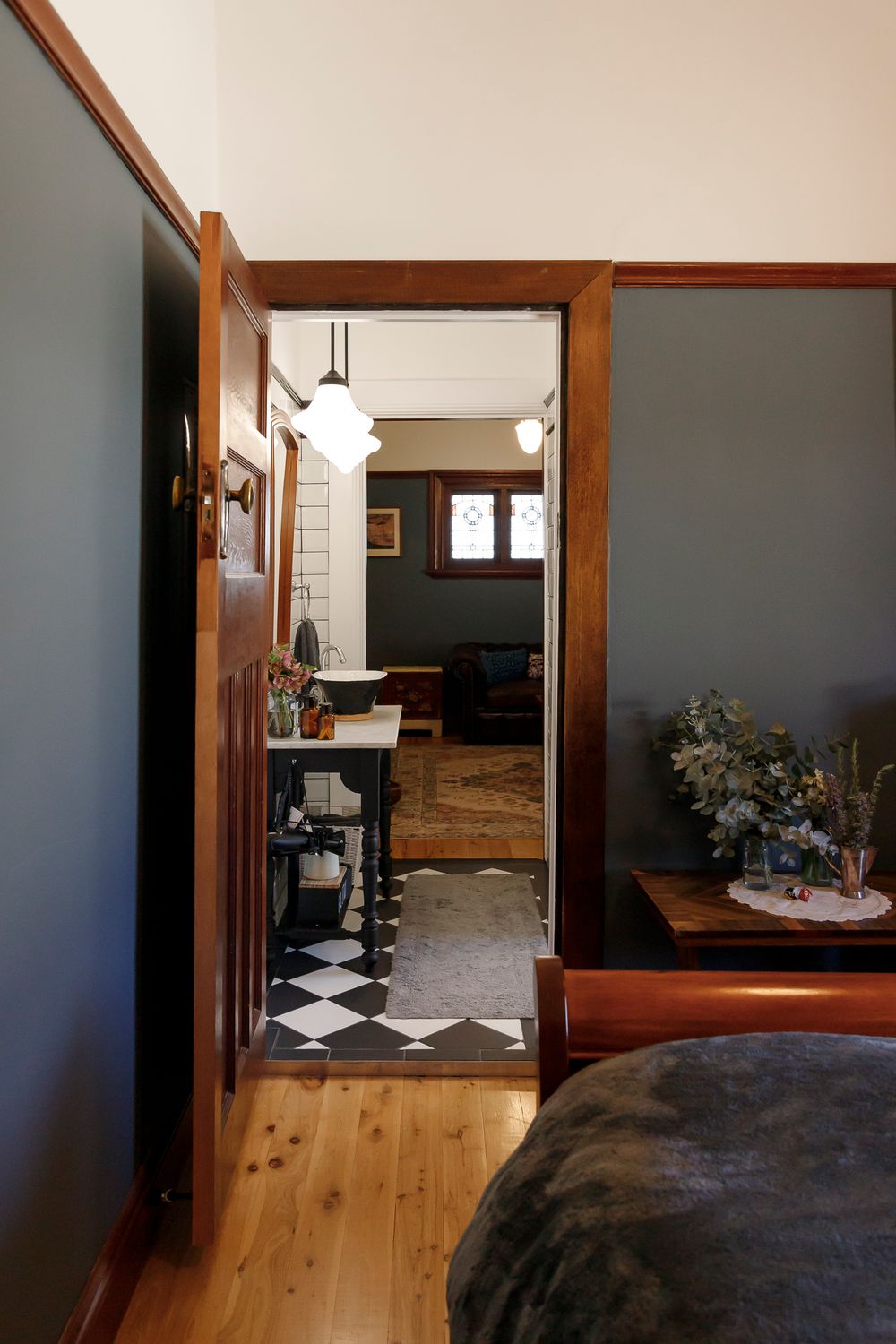 Interior image by Em Callaghan of art deco home with dark blue walls and timber trim, view from bedroom through to the bathroom and lounge.