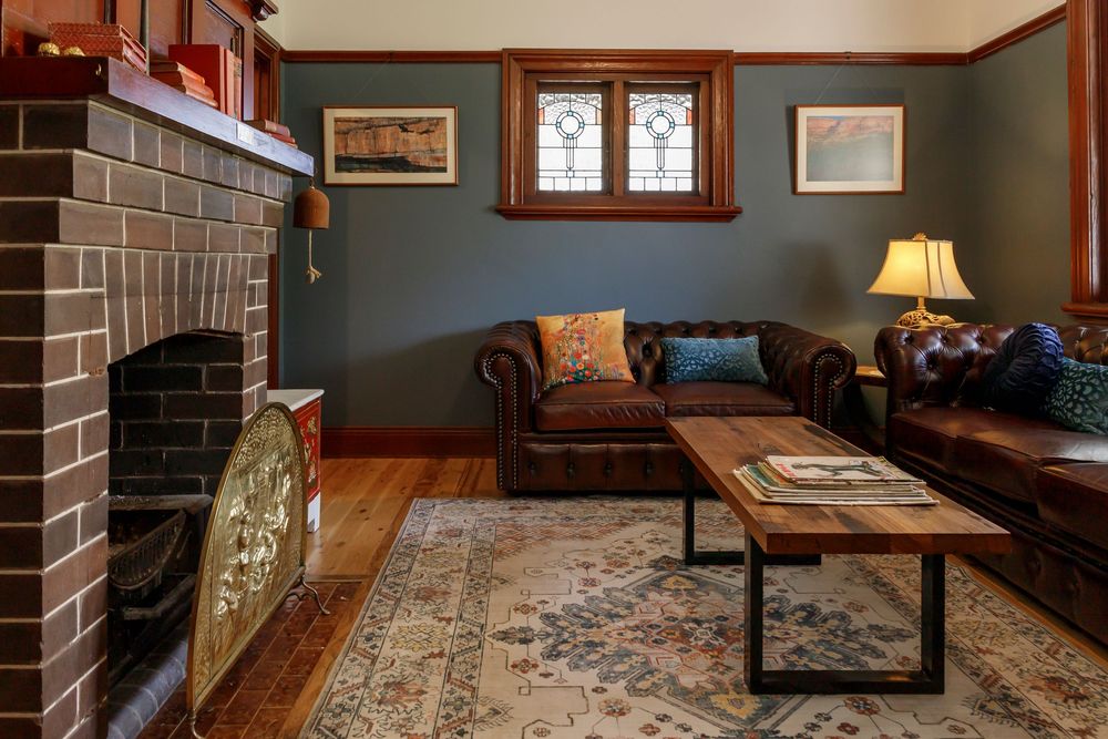Interior property photo by Em Callaghan Photography of an art deco lounge room with dark blue walls, timber trim and brown brick fireplace.