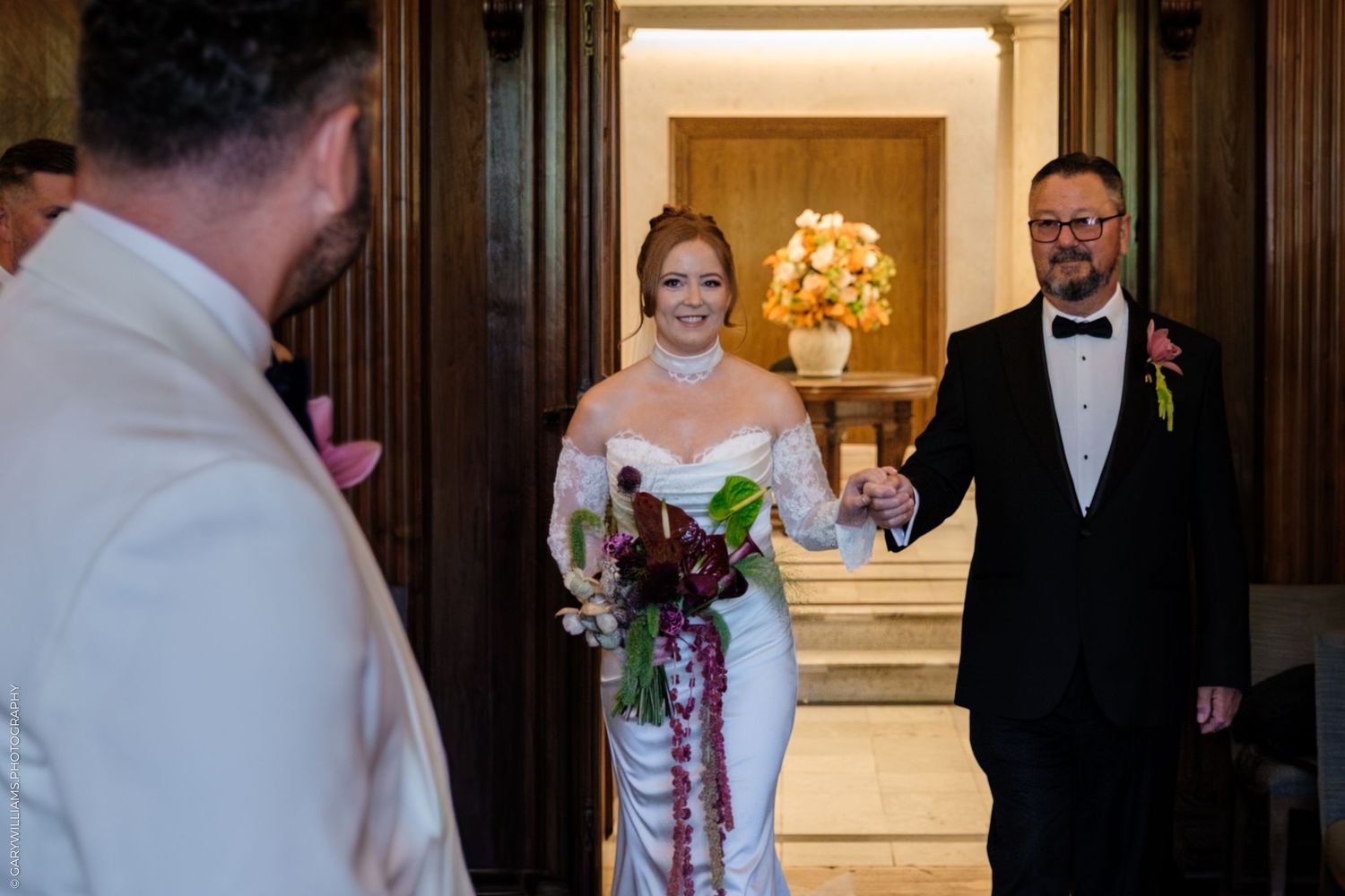 A group stands in formal attire in an elegant ballroom space with grand lighting fixtures and dark wood paneling.