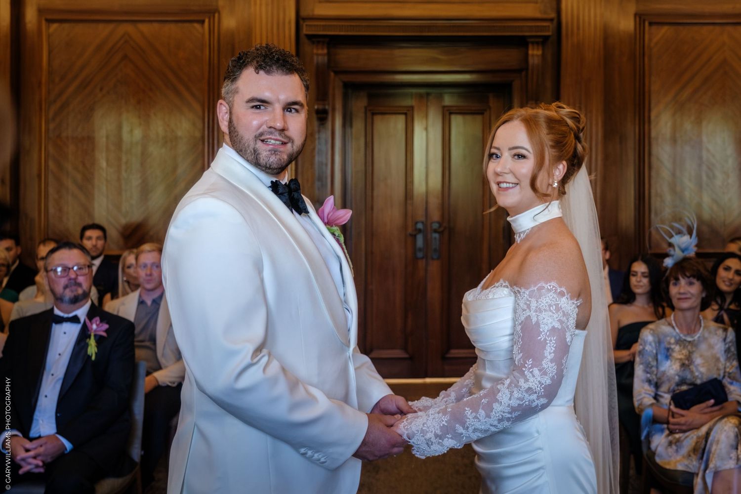 A couple shares their first dance at a wedding reception in an elegant wood-paneled room surrounded by guests.