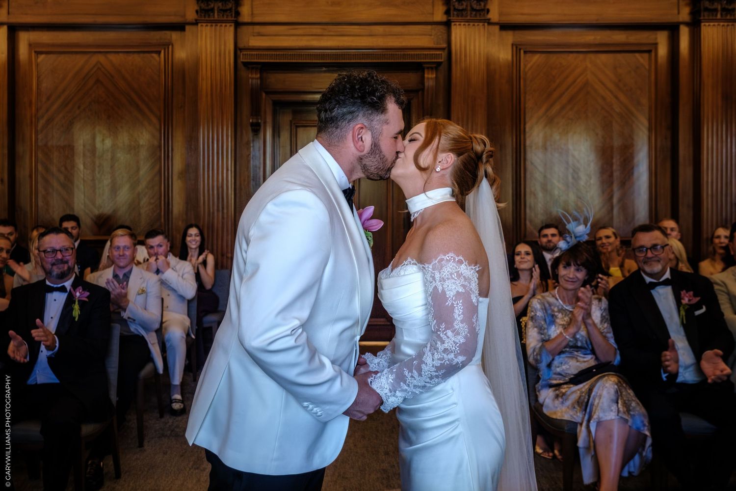 A couple shares a romantic dance with guests looking on in an elegant wedding reception hall with wood paneled walls.