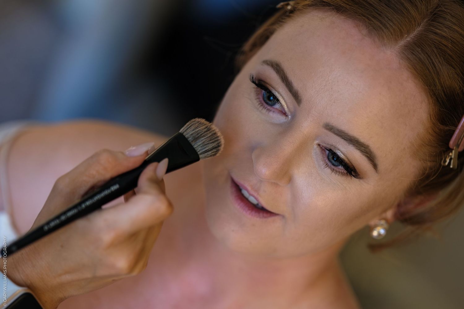 A makeup artist applies powder using a fluffy brush during a wedding beauty preparation session.