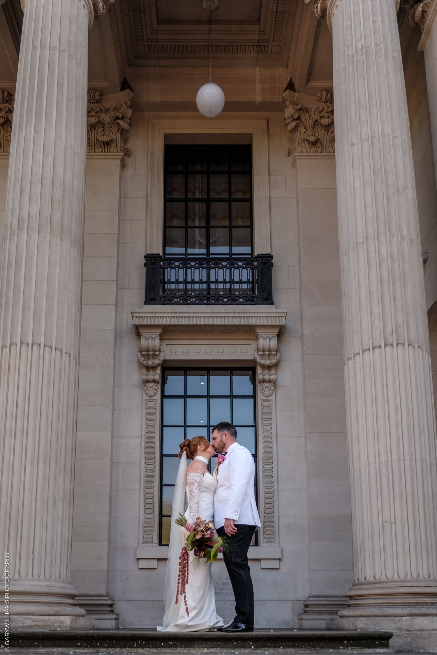 Elegant wedding couple standing between classical stone columns at historic building entrance.