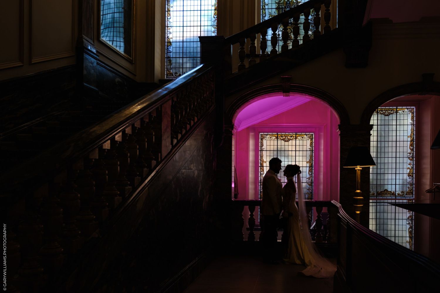 An elegant pink-lit stairwell creates a romantic silhouette effect with two people standing in the illuminated window frame.