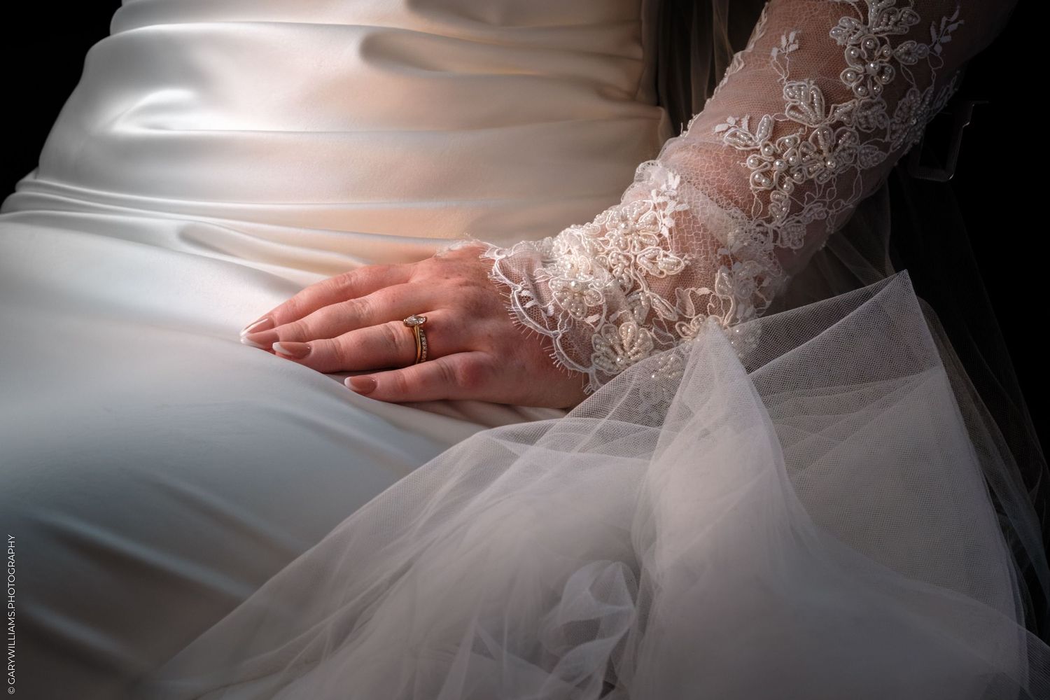Close-up detail of a white lace wedding dress with delicate embroidery and sheer fabric in natural light.