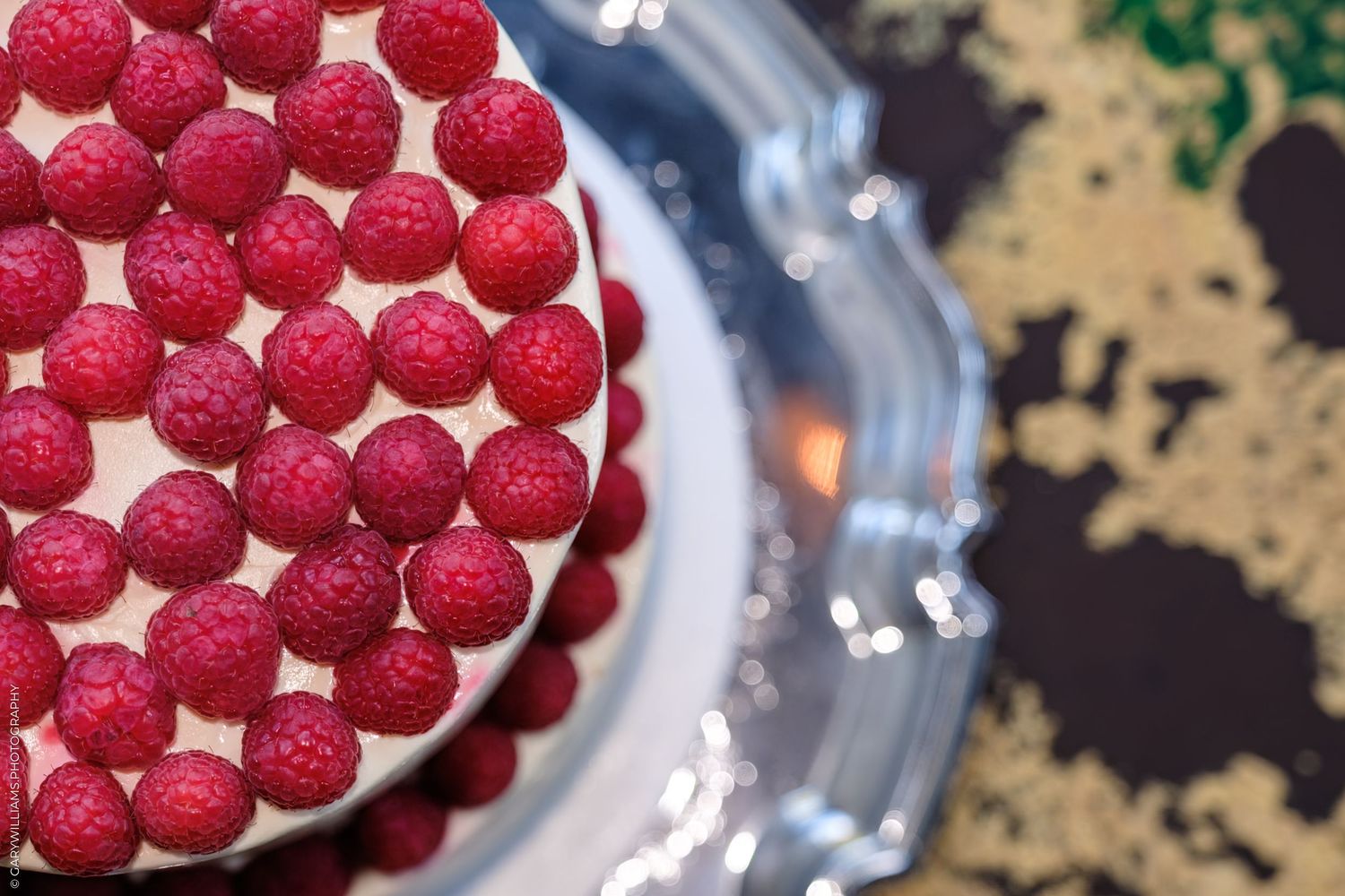 Fresh red raspberry macarons arranged in circular patterns on multiple plates on a rustic surface.