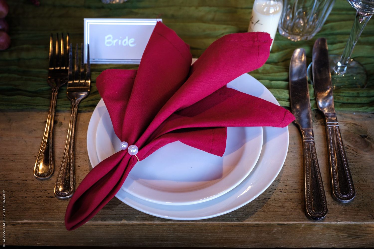 A red folded napkin and white plate with formal place setting on a rustic wooden table.