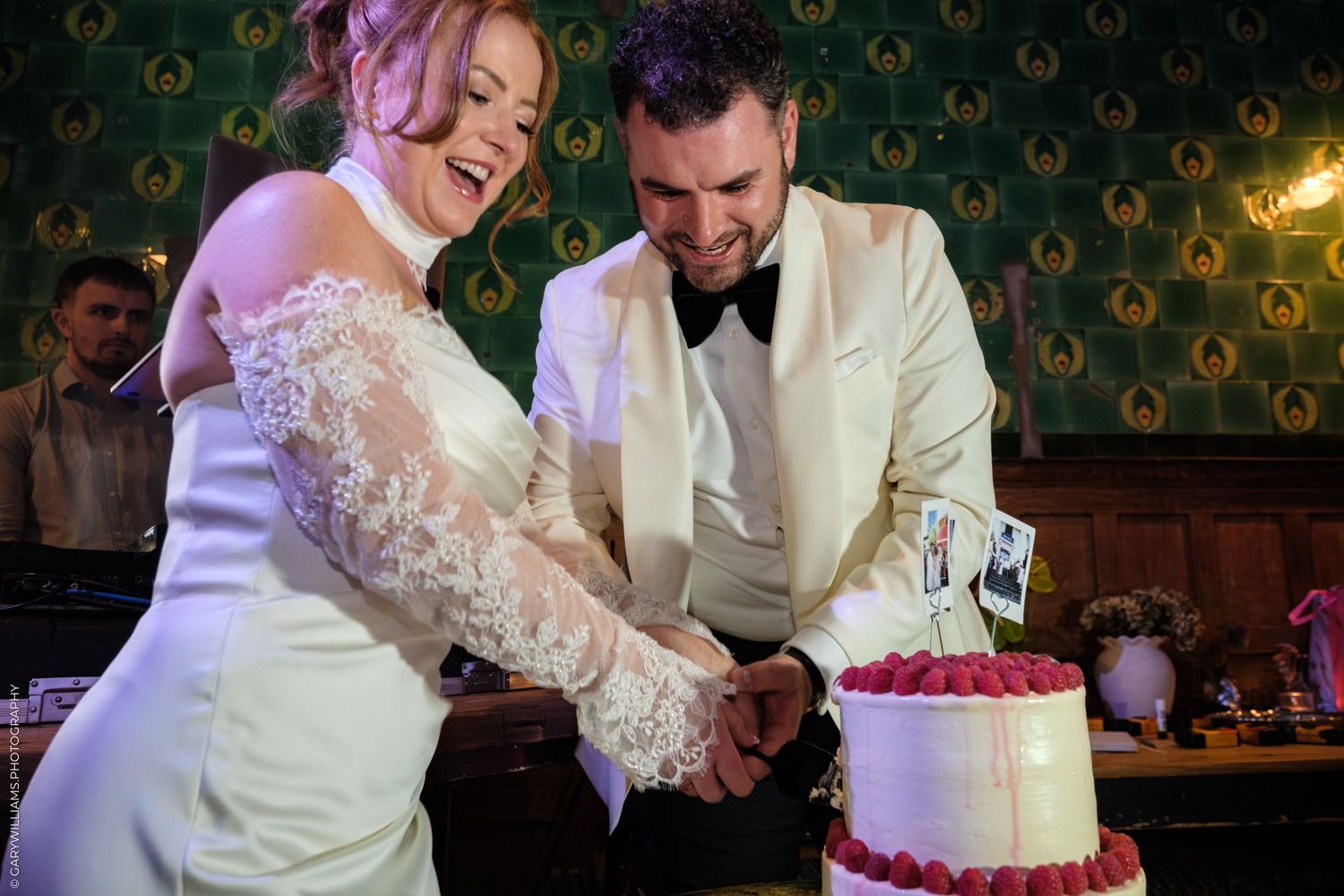 A wedding couple in formal attire share a moment together while cutting their red and white tiered cake.