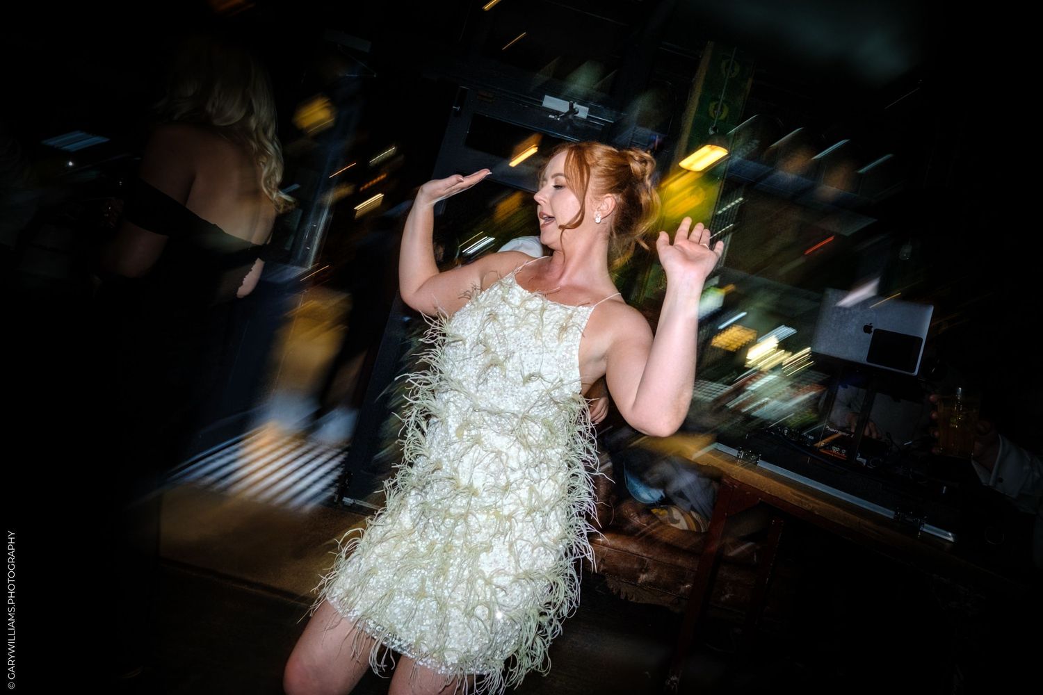 Person in a sparkly white fringe dress dancing energetically at a dimly lit event venue.