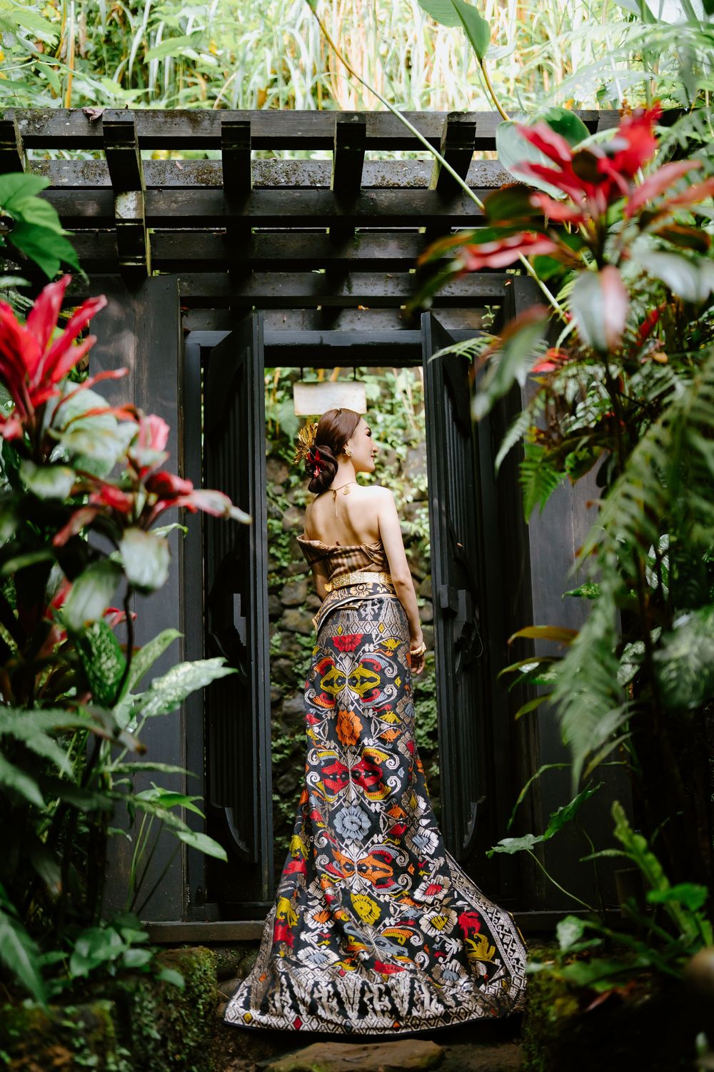 A colorful floral dress flows gracefully in a lush garden setting with a black pergola backdrop.