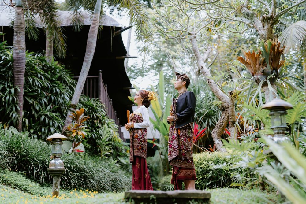 Couple in traditional costumes pose among tropical garden greenery.