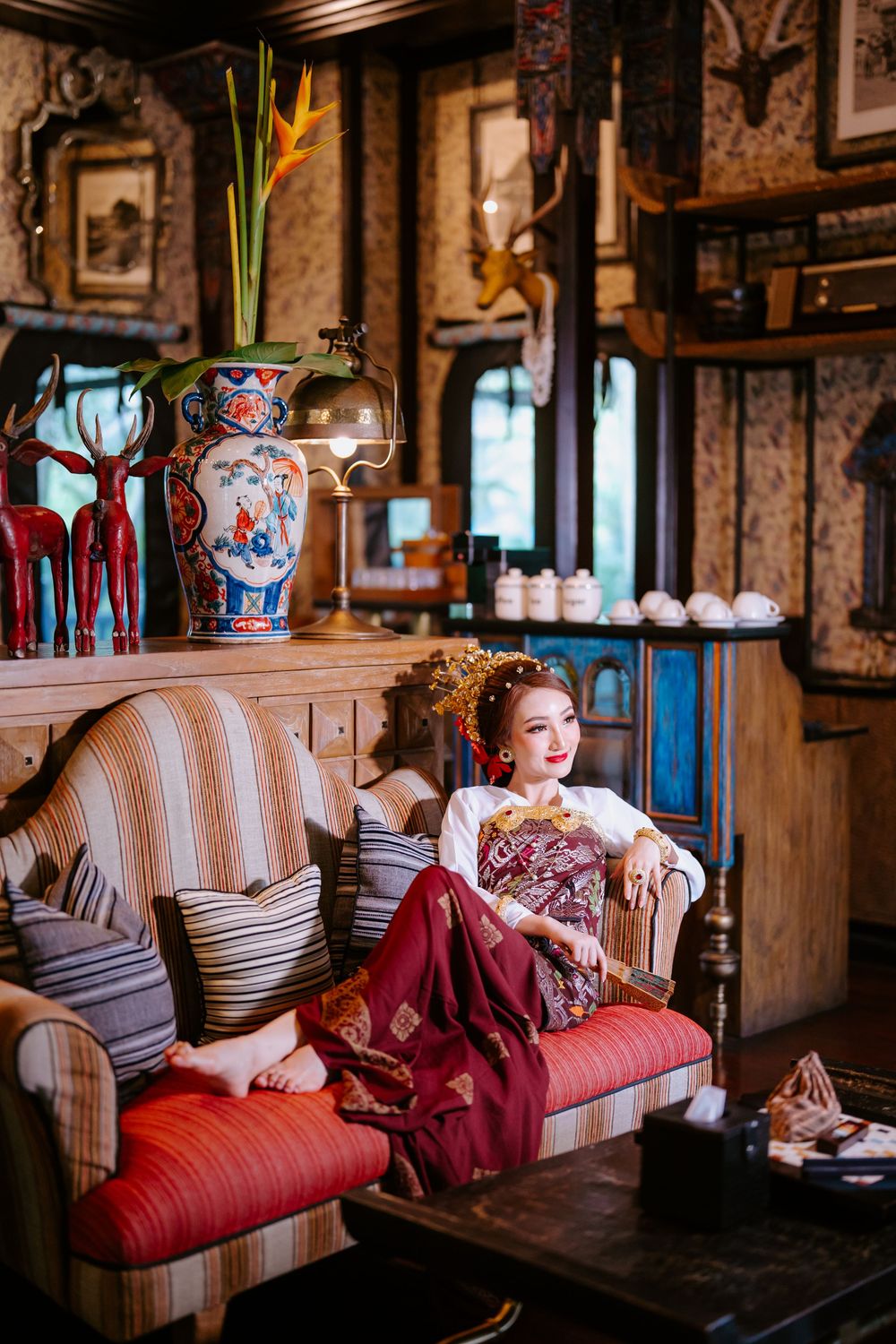 Elegant vintage-inspired scene with burgundy dress and antique furniture in rustic room.