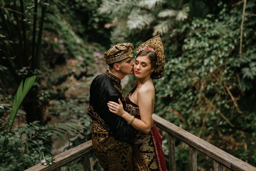A couple in traditional Javanese wedding attire poses together in a lush garden setting.