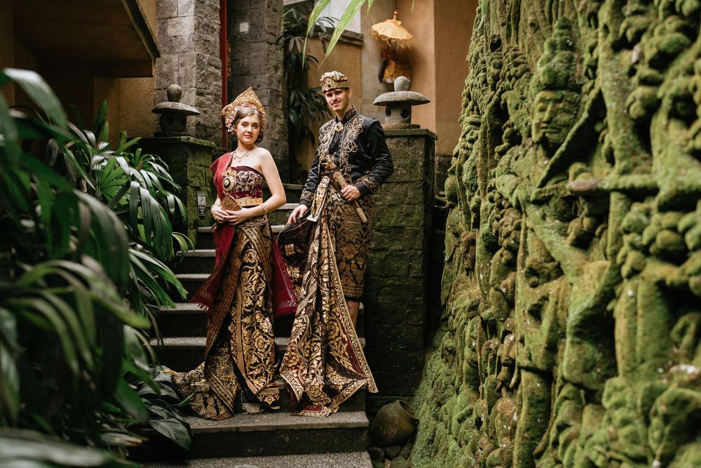 Couple in traditional Balinese wedding attire pose among tropical garden setting.