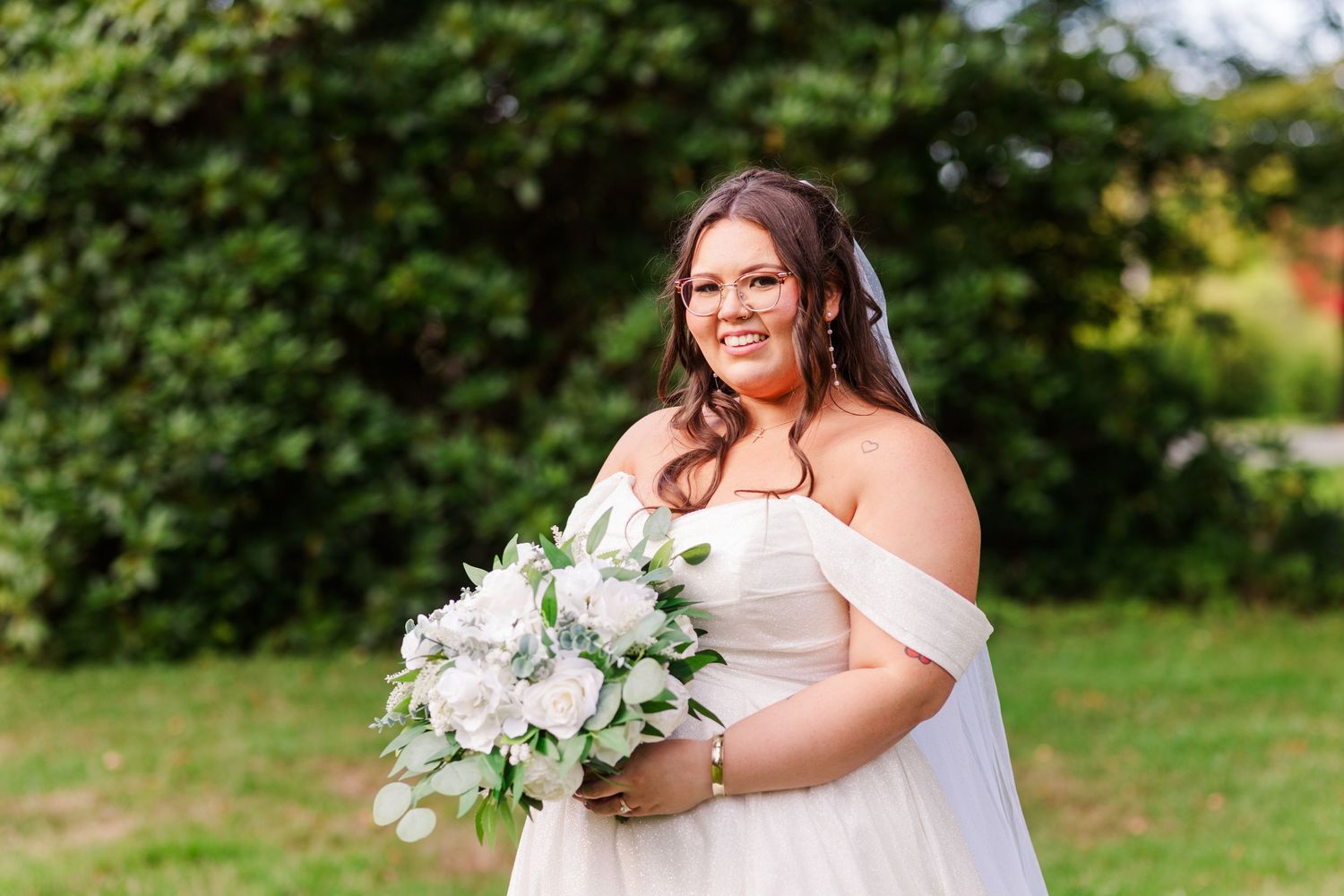 A bride in white dress poses for portraits with her bouquet in a lush garden setting.