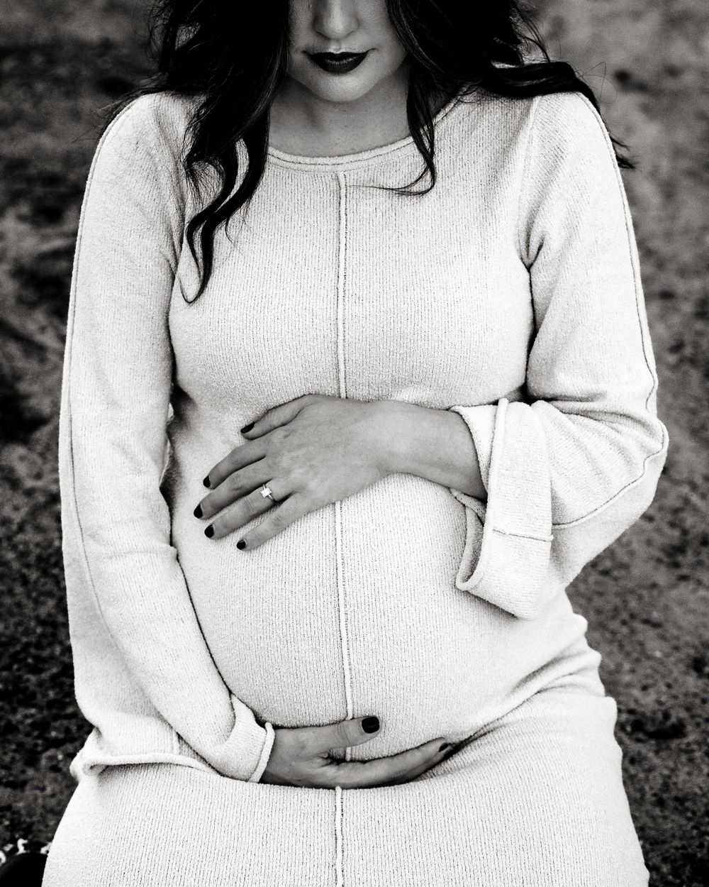 Black and white close-up of pregnant woman in white dress cradling baby bump.