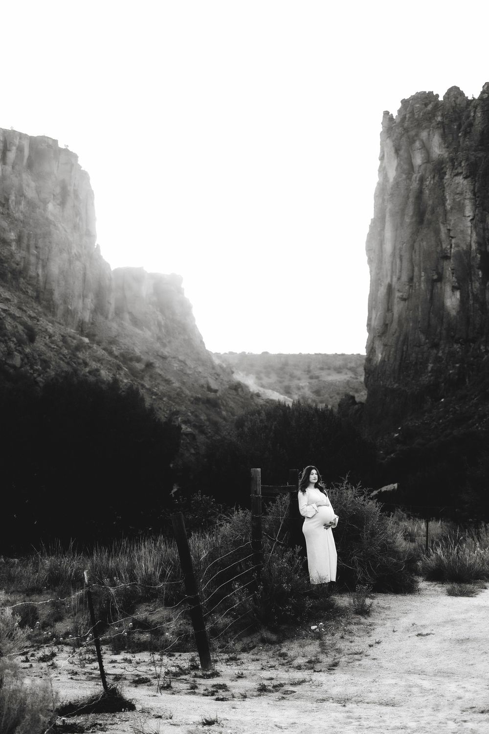 Black and white photo of a woman in a white dress standing between dramatic Diablo canyon rock walls in a New Mexico desert landscape.
