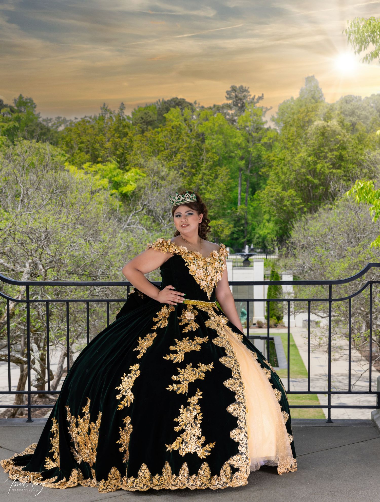 Elegant black and gold ball gown with intricate lace appliques photographed on a balcony at sunset.