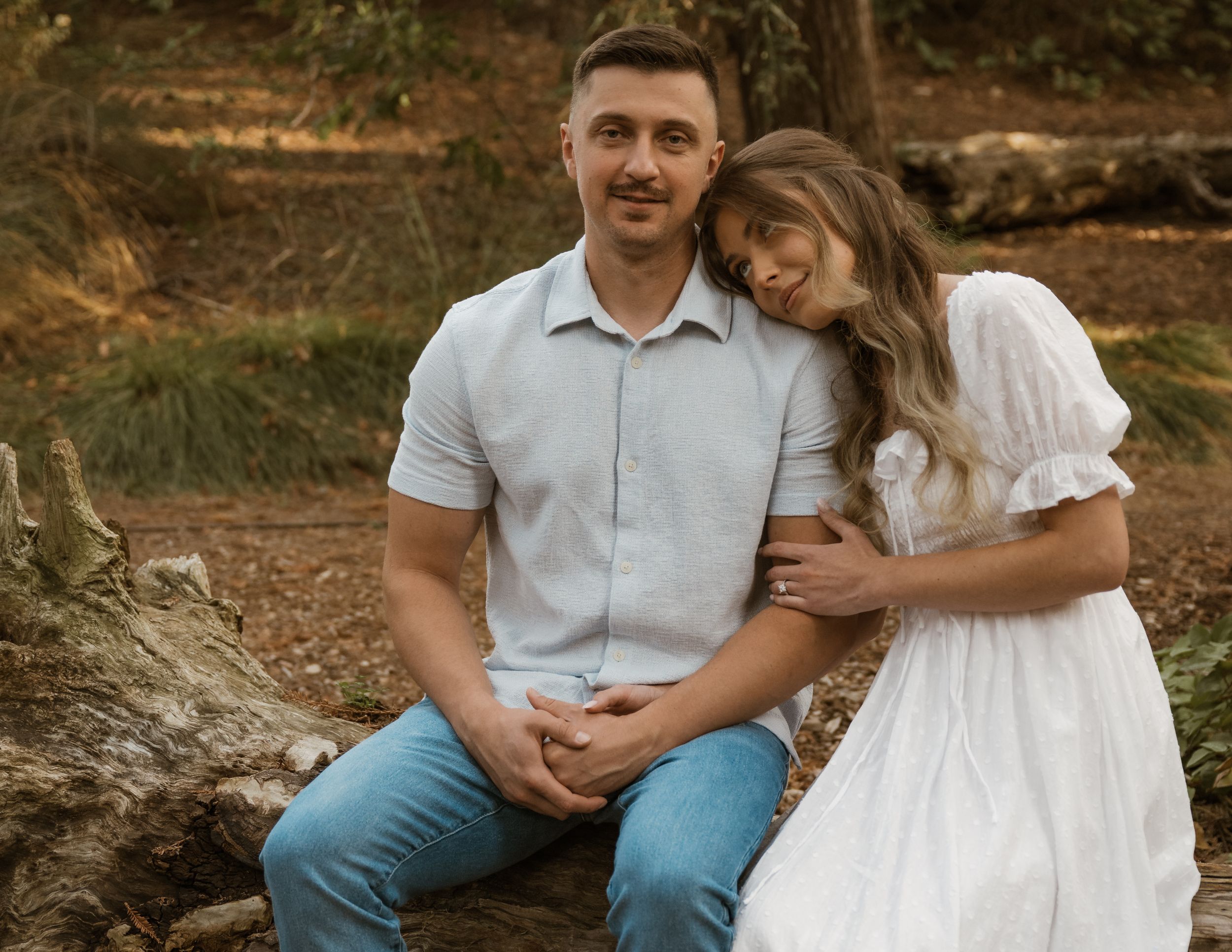 A couple shares tender moments while sitting on a fallen tree in a forest.