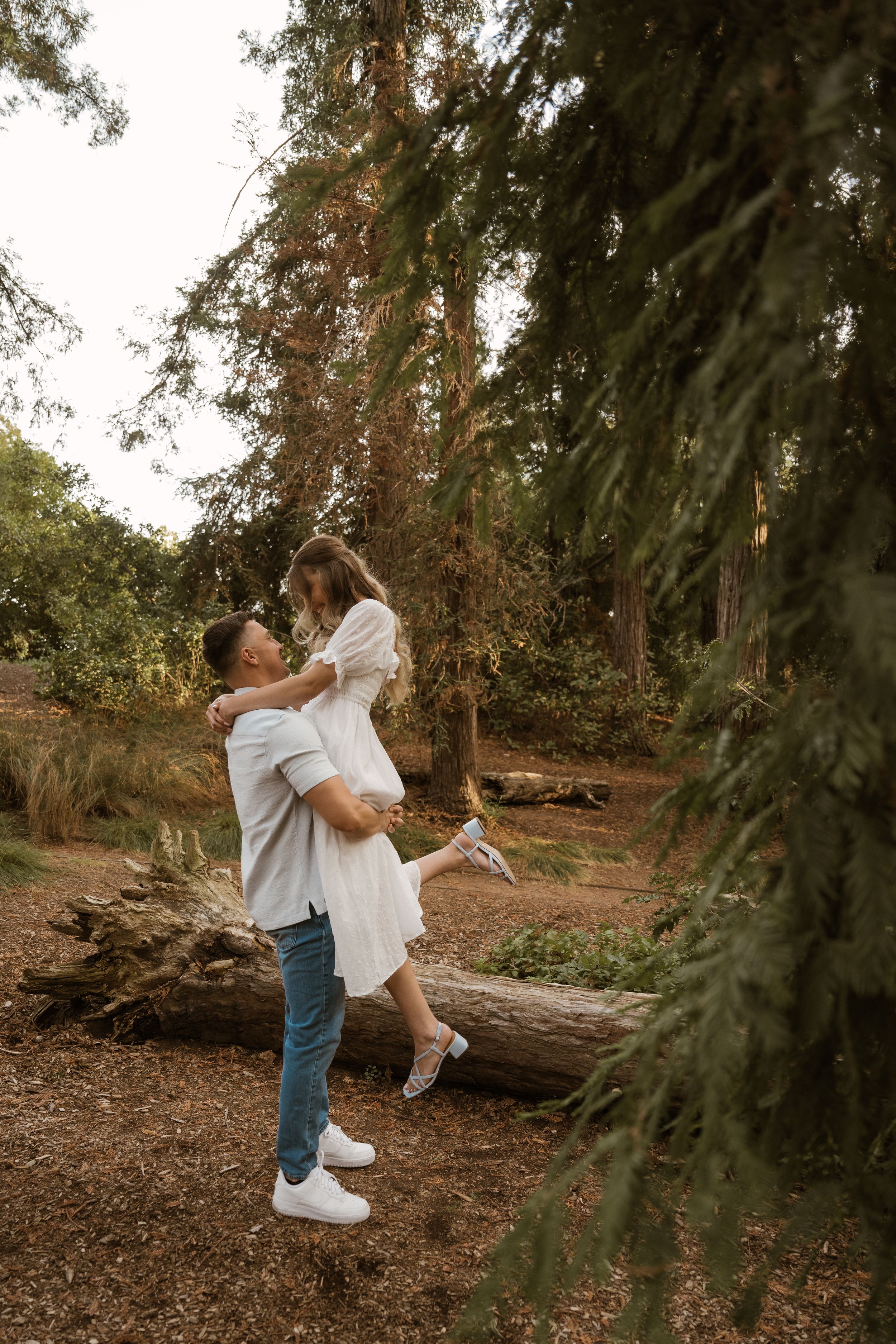 A playful couple dances and spins in a forest clearing at sunset.