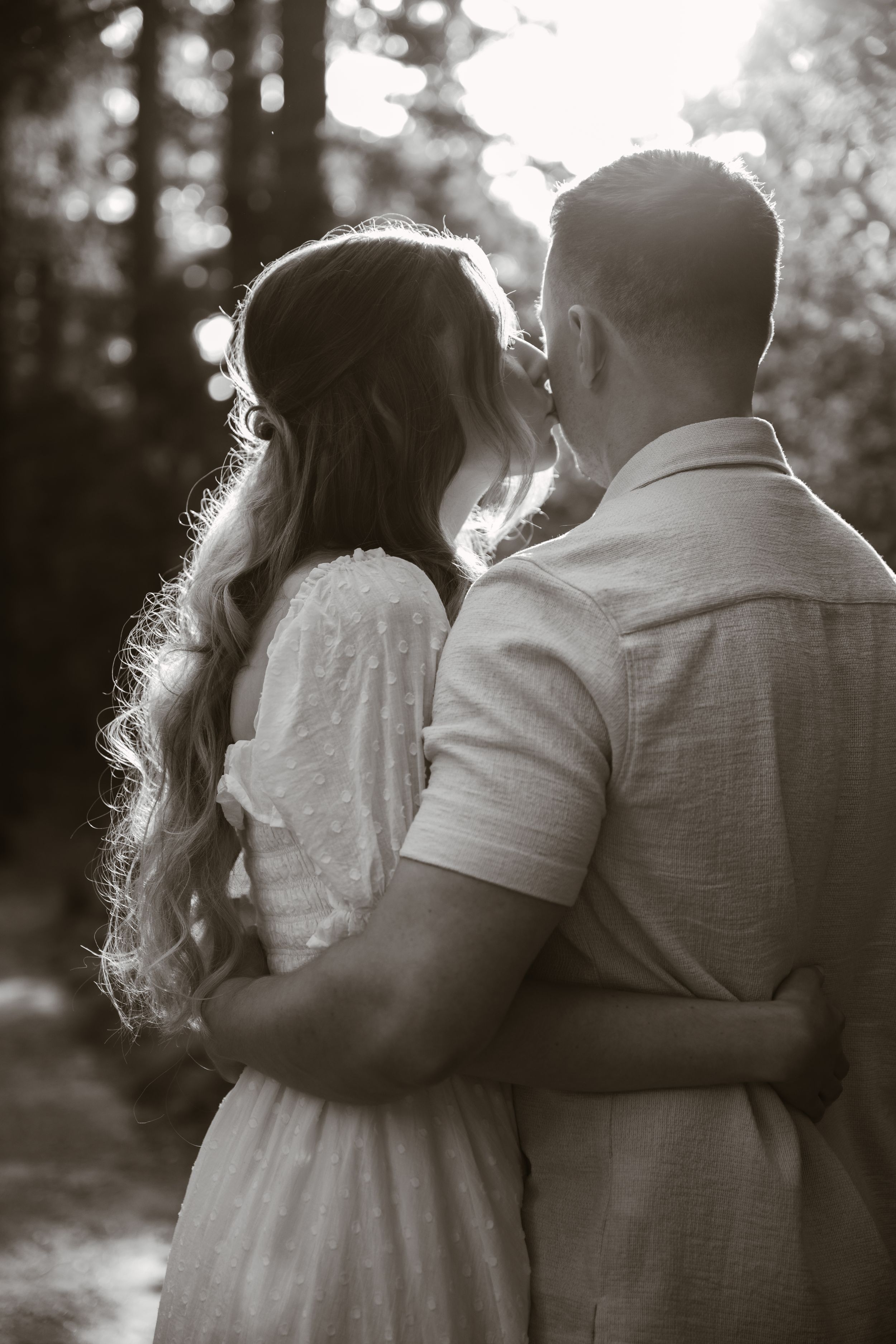A romantic black and white photo series of a couple embracing in a wooded setting.