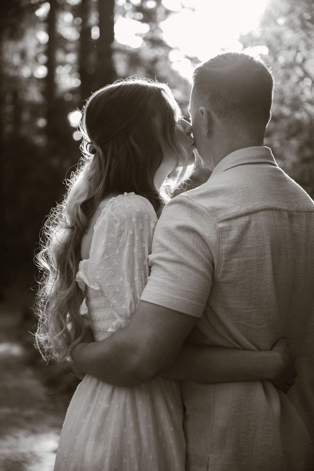 A romantic black and white photo series of a couple embracing in a wooded setting.