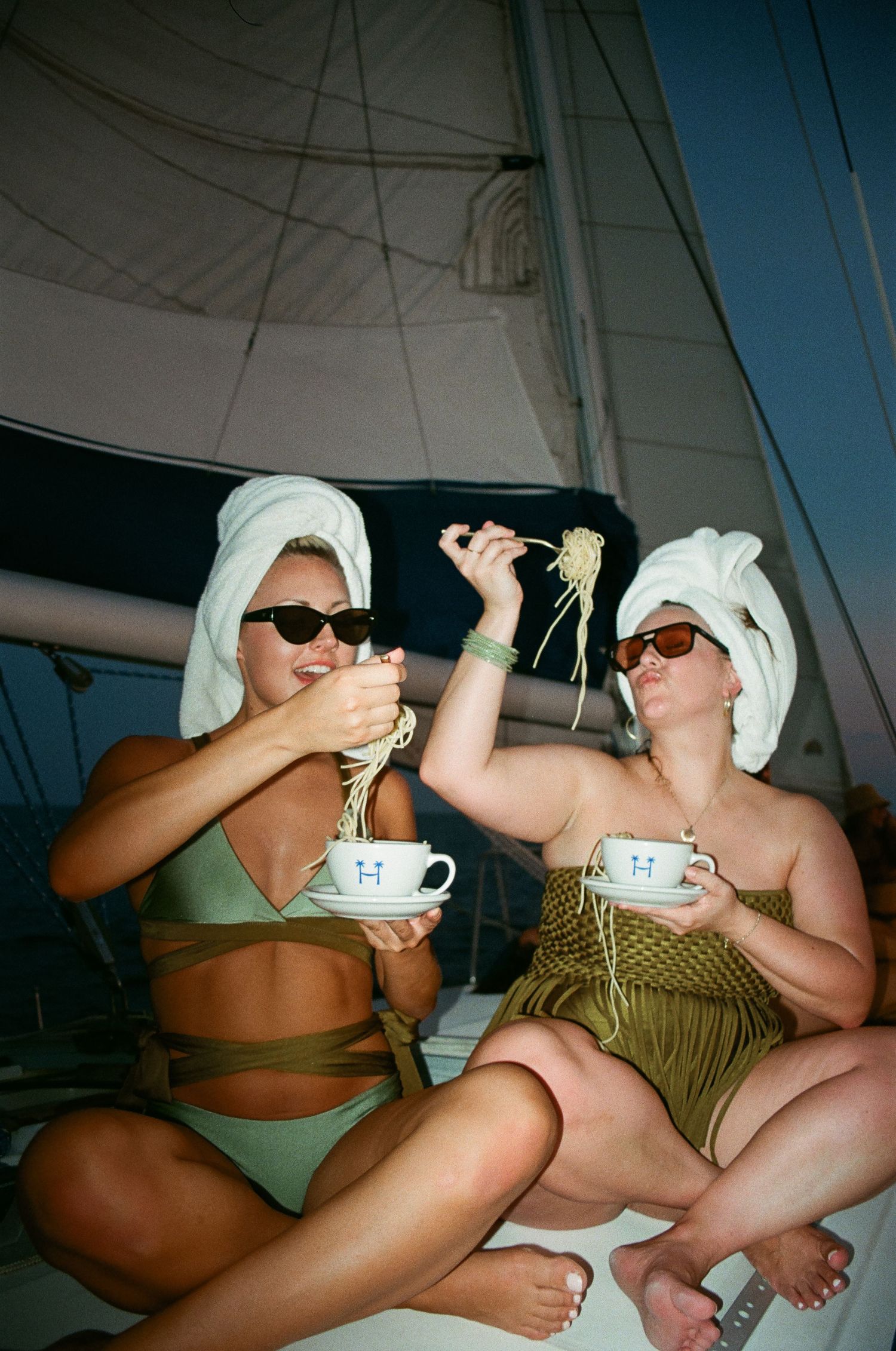 Two people in swimwear and sunglasses relaxing with tea cups on a boat deck.