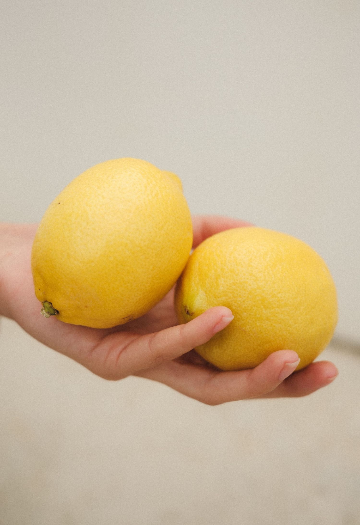 Fresh yellow lemons being held in a hand against a neutral background.