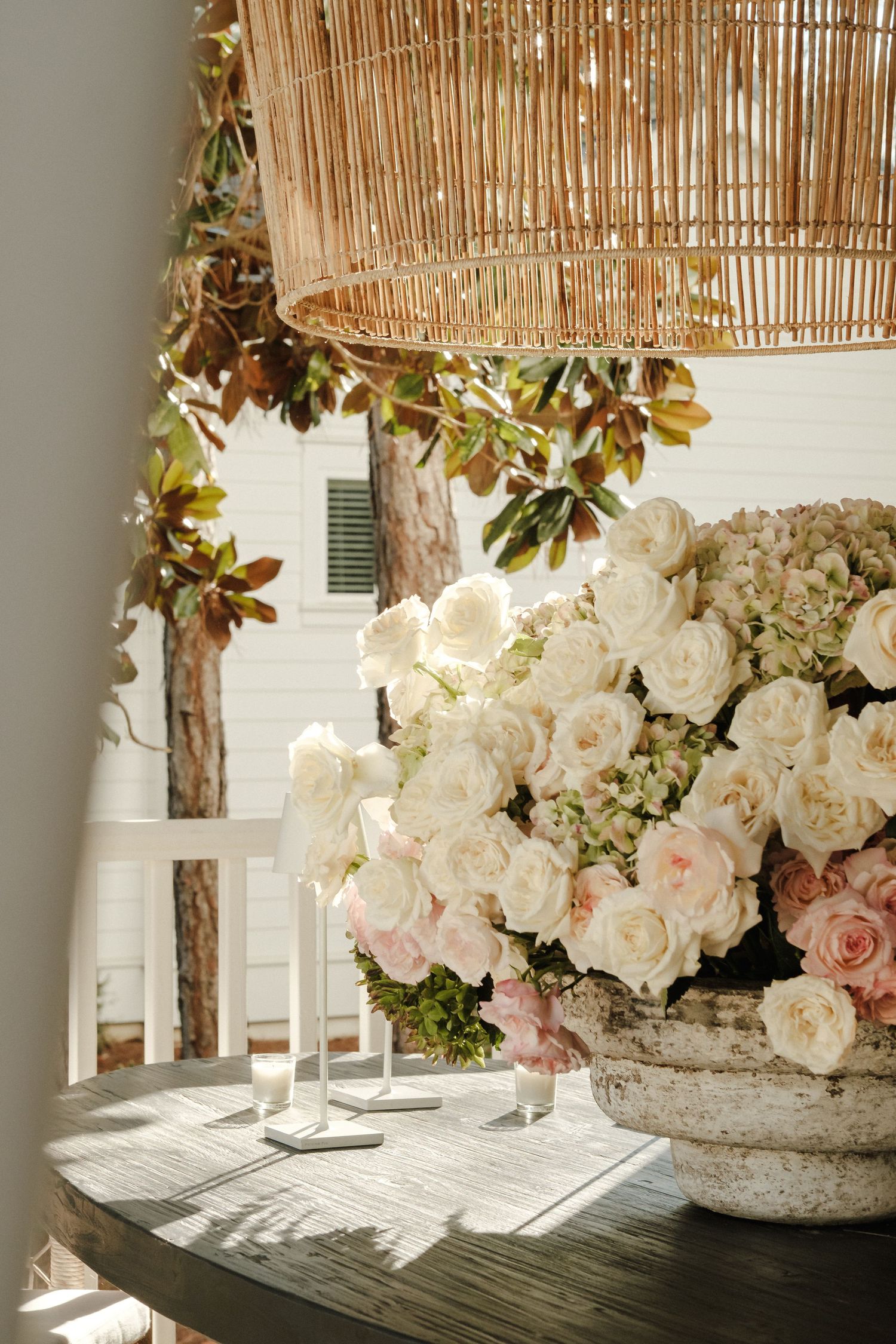 Elegant floral arrangement of white roses in a stone vase under bamboo pendant lighting.
