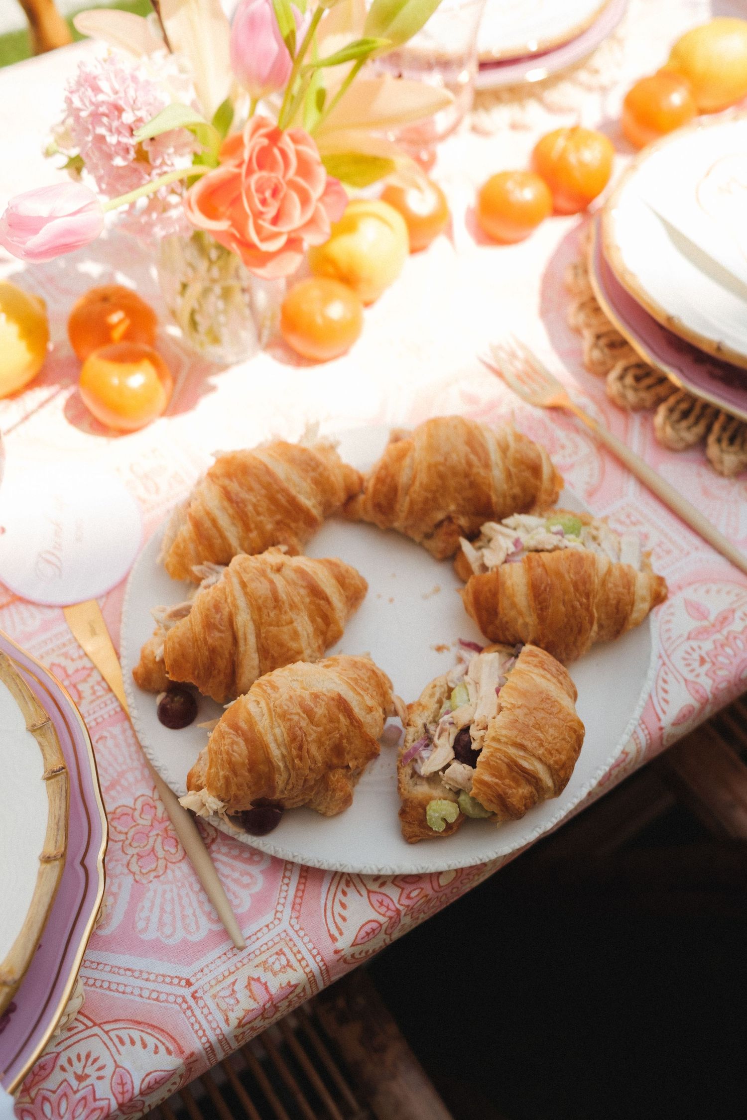 Fresh croissants and citrus fruits arranged on pink patterned tablecloth.