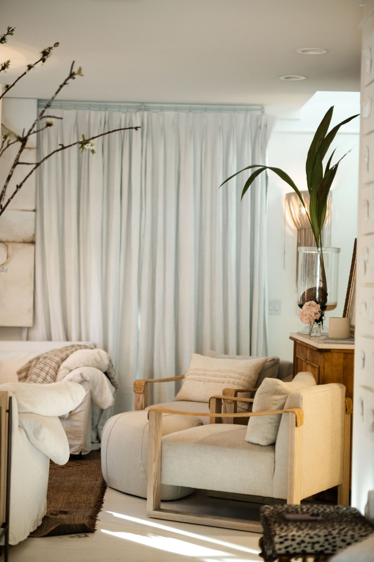 Bright modern living room with white curtains, cozy seating, and decorative plants.