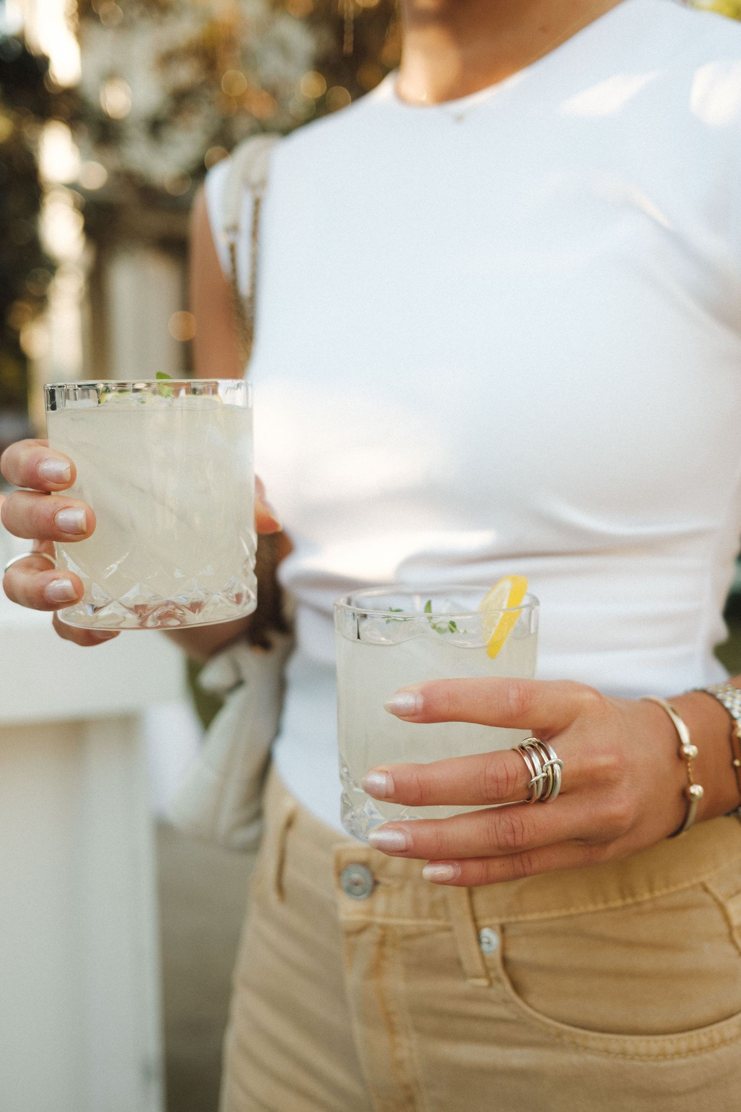 Hands holding frosted cocktail glasses with salt rims against white clothing.