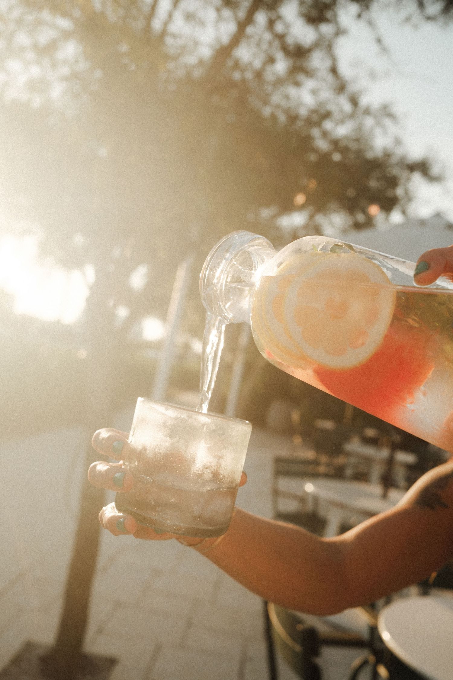 Sunlit glass being filled with a pink cocktail outdoors.