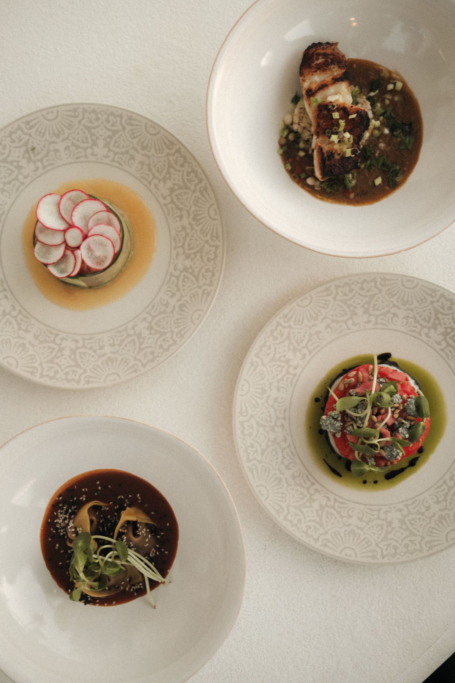 Elegant white plates with beautifully plated appetizers and garnishes on a restaurant table.